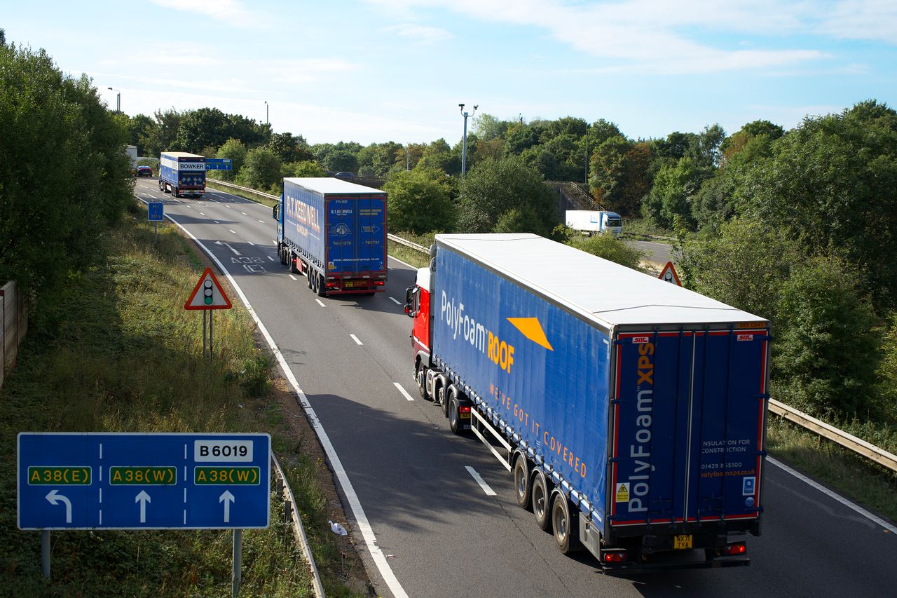 Home Cargo trucks on A38 highway, Mansfield, UK, surrounded by summer greenery and clear skies.