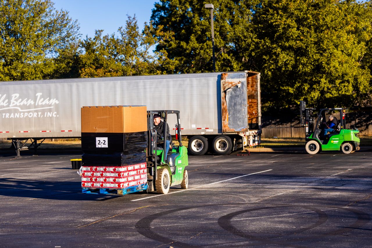 Home Forklift operators loading pallets onto a truck outdoors on a sunny day. Efficient warehouse logistics in action.